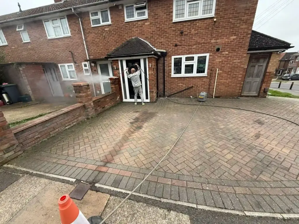 Professional high-pressure jet washing and deep cleaning of a weathered herringbone block paving driveway outside a brick terraced house