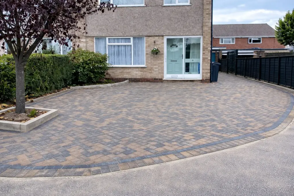 Curved block paved driveway with dark border edging and integrated tree planter leading to a residential house front