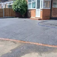 Newly paved black asphalt front driveway finished with a neat red brick header course border, wooden fencing, and a brick pillar front wall