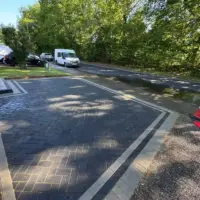 Newly installed dark charcoal block paving driveway featuring a herringbone pattern, contrasting border edging, and a paved threshold leading out to a residential road