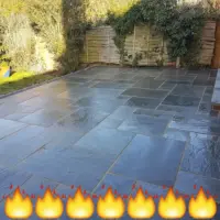 Sleek dark grey slate flagstone patio installation featuring precision-pointed joints, a neat brick-edged step, and an adjoining garden bordered by wooden fencing and ivy-covered greenery