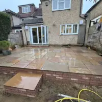 Elevated multi-toned Indian sandstone patio featuring a sturdy brick retaining wall, matching stone step block, and French doors leading out from a rendered residential house