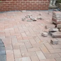 Red clay brick paving in a herringbone pattern with a dark curved soldier course border, following the line of a red brick retaining wall during garden construction