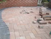 Red clay brick paving in a herringbone pattern with a dark curved soldier course border, following the line of a red brick retaining wall during garden construction