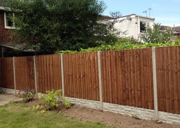 Newly stained brown wooden lap fence panels fitted between durable concrete posts and textured patterned concrete gravel boards, bordering a residential lawn and garden bed
