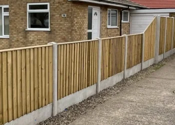 Stepped featheredge wooden fencing with concrete posts and gravel boards running alongside a concrete driveway and a residential yellow-brick bungalow