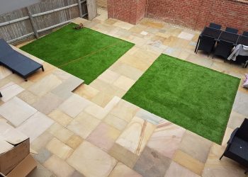 Contemporary multi-level garden design featuring varied sandstone flagstone paving, integrated artificial grass lawn sections, outdoor patio furniture, and traditional brick retaining walls