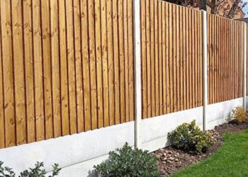 Modern vertical timber slat fence panels installed with sturdy concrete posts and smooth concrete gravel boards above a garden bed and green lawn